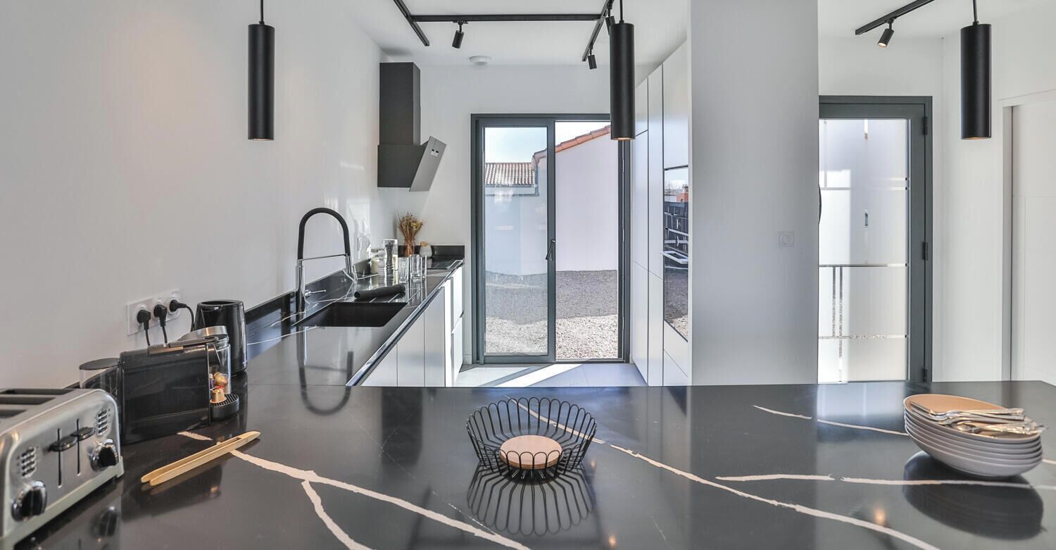 Una cucina moderna con isola centrale, zona pranzo con una sedia particolare e vista esterna.