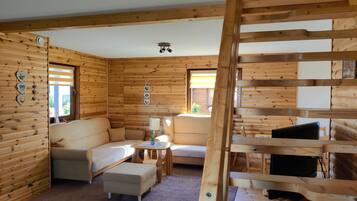 A log cabin interior with a sofa, armchair, ottoman, and a television on a wooden stand.