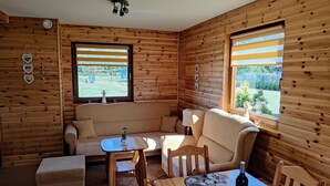 A cozy cabin interior with a sofa, dining table, and two windows with blinds. - Large, Comfortable Holiday Home With a Garden (Smoldzino)