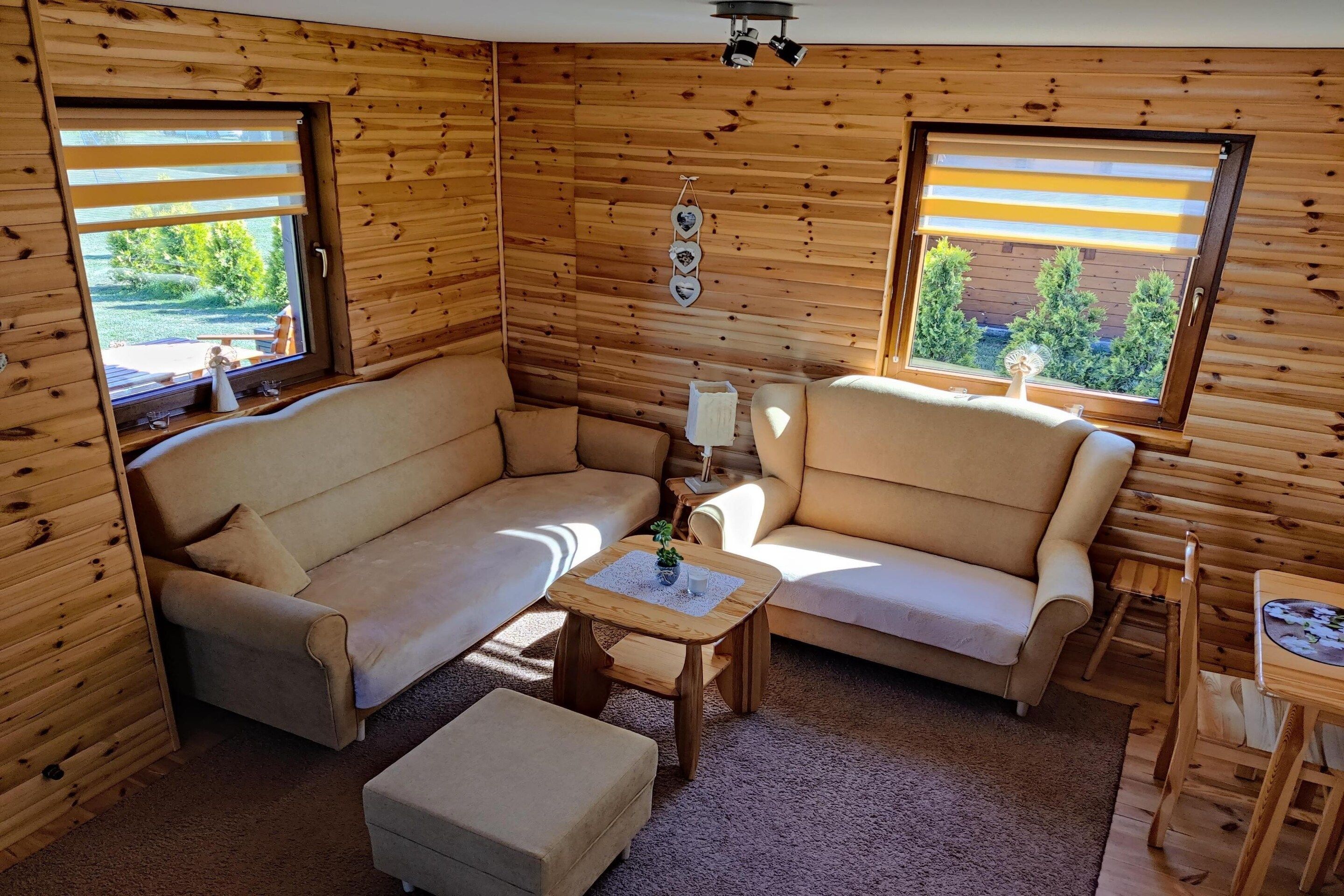 Un interior de cabaña acogedor con sofá, sillón, reposapiés y una mesita.