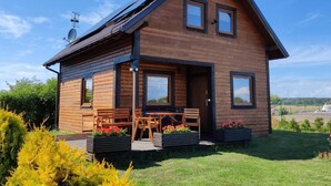 A modern log cabin with a sloped roof, large windows, and a patio with outdoor furniture. - Large, Comfortable Holiday Home With a Garden (Smoldzino)