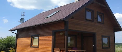 A wooden cabin with a sloped roof, a satellite dish, and a small porch with outdoor seating.