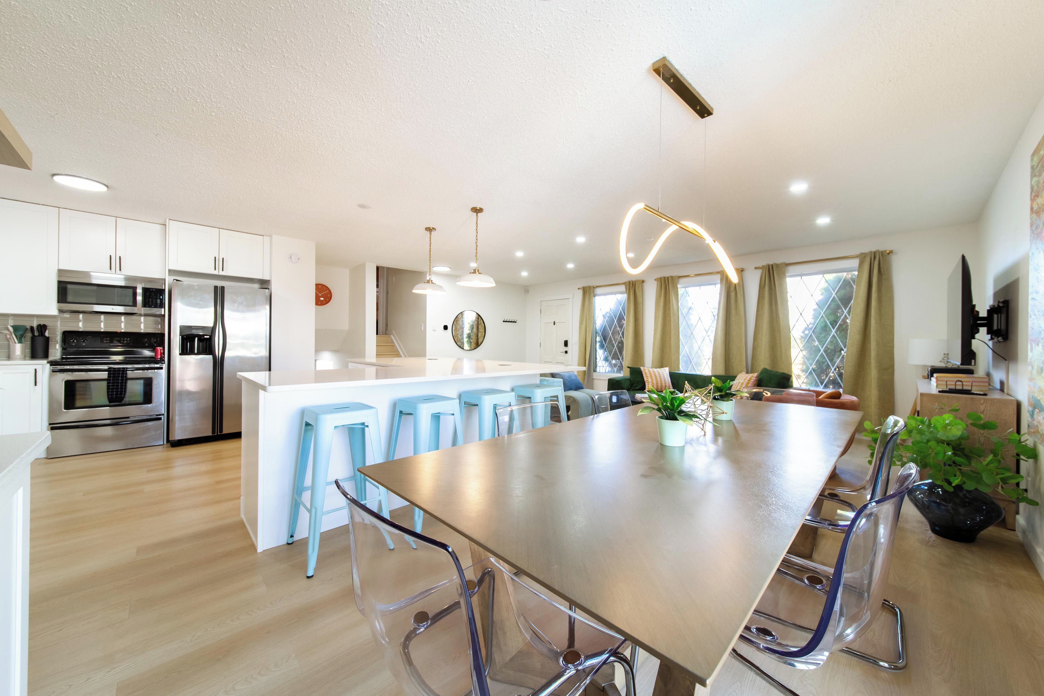 A modern kitchen with stainless steel appliances, a central island with stools, and a dining area with a large table.