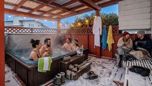 A hot tub area with a wooden deck, a covered seating area, and a view of houses in the background. - Renovated retreat in NE Edmonton with a sauna, Pac-Man & Street Fighter arcade, home theater with projector & popcorn machine. 16 min to downtown, 8 min to Rundle Park golf. Built for families, friend groups & celebrations up to 13 guests. (Edmonton)