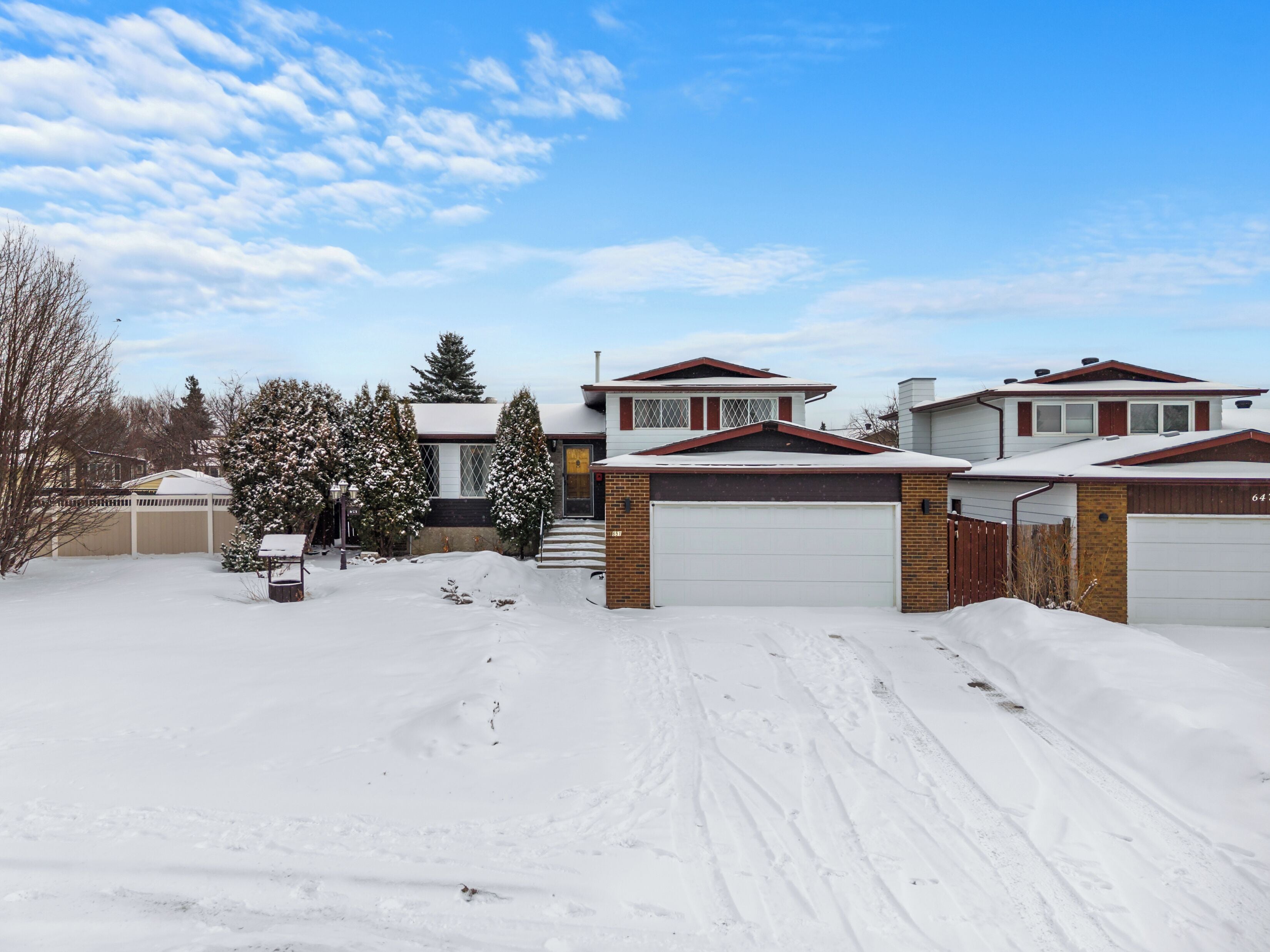 A residential area with houses, a snow-covered driveway, and a clear sky.