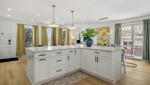 A modern kitchen with white cabinetry, pendant lighting, and a large island. - Renovated retreat in NE Edmonton with a sauna, Pac-Man & Street Fighter arcade, home theater with projector & popcorn machine. 16 min to downtown, 8 min to Rundle Park golf. Built for families, friend groups & celebrations up to 13 guests. (Edmonton)