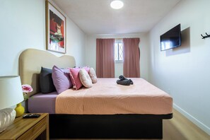 Een slaapkamer met een bed, een televisie, een raam met gordijnen en een schilderij aan de muur.