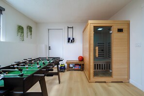 A room with a foosball table, a sauna, and a small table with toys and a basketball. - Older home in NE Edmonton with a renovated retro interior: hot tub, sauna, Pac-Man & Street Fighter arcade, home theater with projector & popcorn machine. 16 min to downtown, 8 min to Rundle Park golf. Pool closed for the season. Up to 12 guests. (Edmonton)