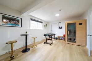 Una habitación con mesa de futbolín, un cuadro con una escena de piscina y una puerta de madera.