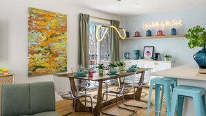 A modern kitchen with a dining area, a neon sign, and a large abstract painting. - Renovated retreat in NE Edmonton with a sauna, Pac-Man & Street Fighter arcade, home theater with projector & popcorn machine. 16 min to downtown, 8 min to Rundle Park golf. Built for families, friend groups & celebrations up to 13 guests. (Edmonton)