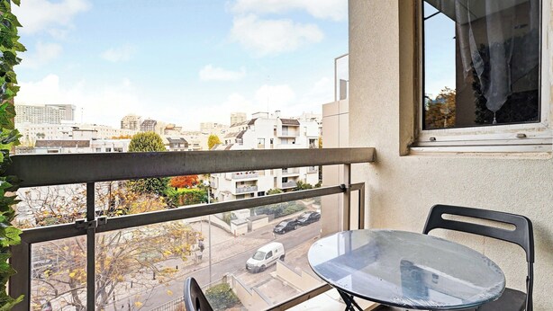 Un balcon avec une table et des chaises, une vue sur le paysage urbain et une fenêtre avec un rideau.