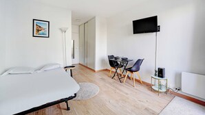 Une chambre à coucher comprenant un lit, un bureau, une chaise, une télévision et une petite table avec un haut-parleur.