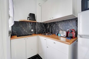 A compact kitchen with a black marble backsplash, white cabinets, a stainless steel sink, and a red espresso machine. - Charming Studio 2P - Courbevoie (Courbevoie)