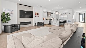 A modern living room with a large sectional sofa, a flat-screen TV, and a fireplace. - Luxury 4-bedroom house in a family-friendly Houston neighborhood (Houston)