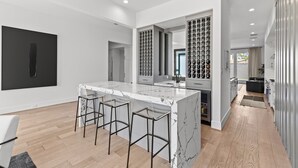 A modern kitchen with a marble island, bar stools, and wine storage. - Luxury 4-bedroom house in a family-friendly Houston neighborhood (Houston)