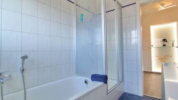 Un baño con bañera, ducha y zona de ducha con mampara de vidrio.