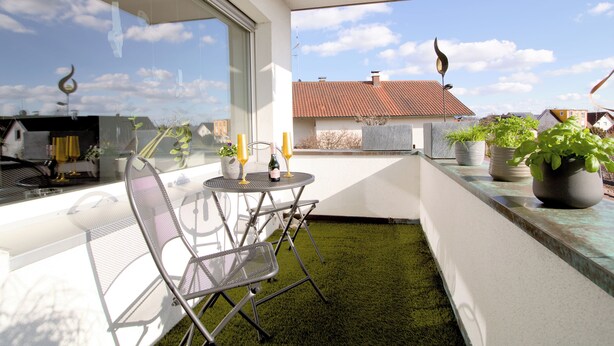Ein Balkon mit Stuhl, Tisch und Blumentopf.