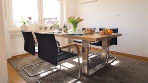 Ein Essbereich mit Tisch, Stühlen, einer Blumenvase und einer Obstschale.