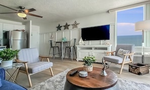 Ein modernes Wohnzimmer mit Flachbildfernseher, Sitzgelegenheiten, Deckenventilator und Meerblick.
