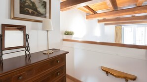 Een houten dressoir met lades, een spiegel, een lamp, een kleine potplant en een houten plank aan een witte muur.