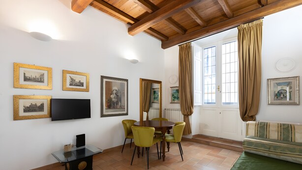 Een eetgedeelte met een tafel en stoelen, een televisie aan de muur en ingelijste foto's.
