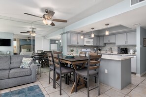 A modern kitchen with a dining area, grey cabinetry, a central island, and a ceiling fan. - Sea Vista Paradise - Beachfront Corner Unit (South Padre Island)