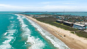 Vista aérea de uma área costeira com praia, edifícios e um píer.