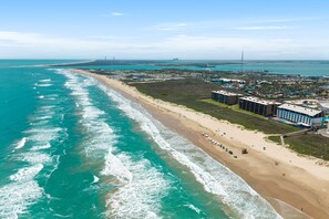 An aerial view of a coastal area with a beach, buildings, and a pier. - Sea Vista Paradise - Beachfront Corner Unit (South Padre Island)