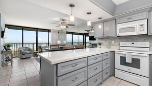 Uma cozinha moderna com uma ilha grande, eletrodomésticos brancos e uma varanda com vista.