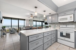 A modern kitchen with a large island, white appliances, and a balcony with a view. - Sea Vista Paradise - Beachfront Corner Unit (South Padre Island)