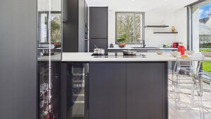 Een moderne keuken met een groot raam, donkere kasten en een bar met transparante stoelen.