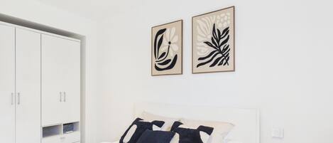 Ein modernes Schlafzimmer mit einem Bett, einem weißen Kleiderschrank und zwei abstrakten Wandbildern.