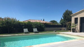 A rectangular swimming pool with two lounge chairs, a tiled deck, and a building with a tiled roof in the background. - House with swimming-pool in Luberon (Lauris)