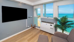 Een moderne woonkamer met een flatscreen-tv, grote ramen met uitzicht op zee, en een plafondventilator.