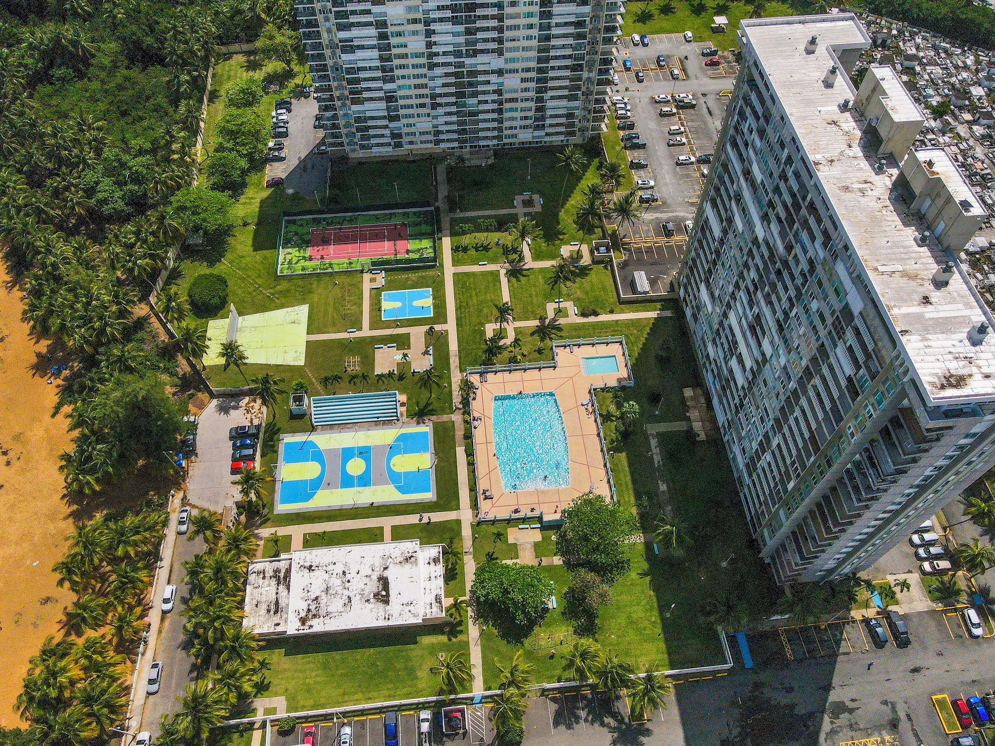 Vista aérea de una zona residencial con edificios altos, una piscina, canchas de tenis y un estacionamiento.
