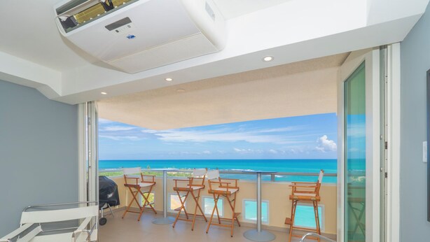 Een balkon met uitzicht op de oceaan, een barbecue en opklapbare stoelen.