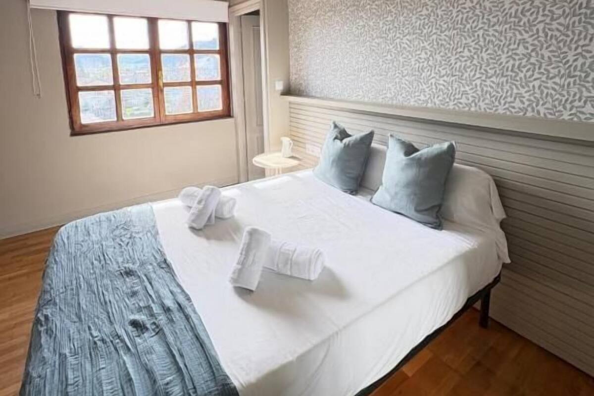 A hotel room with a bed, a window, a patterned wall, and a ceiling light.
