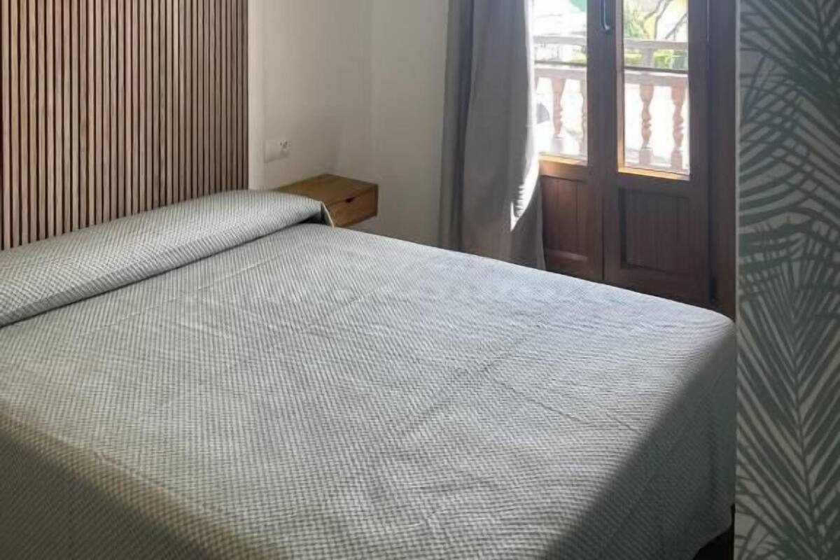 A bedroom with a bed, a wooden slat wall, a small bedside table, and a window with curtains.