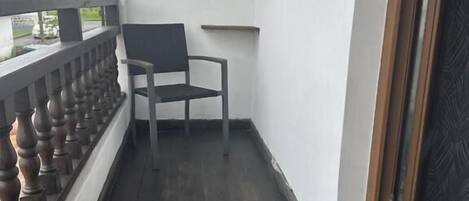 A balcony with a chair, a wooden railing, and a view of the outside.