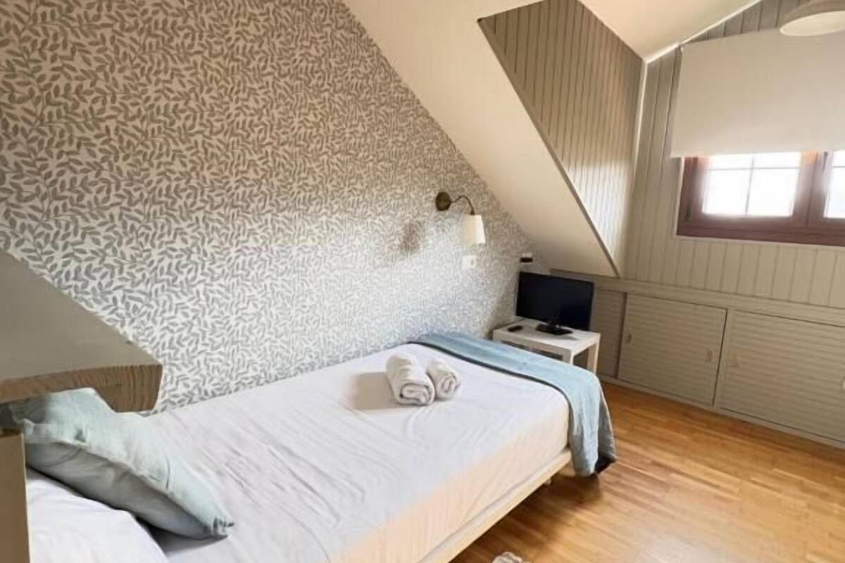 A bedroom with a bed, a nightstand, a TV, a window, and a patterned wall.