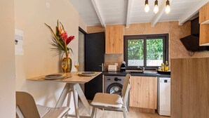 A compact kitchen with a washing machine, a window with a view of greenery, and a dining area with a table and chairs. - Résidence Dorée - Seven Bedroom Villa, Sleeps 14 (Sainte-Anne)