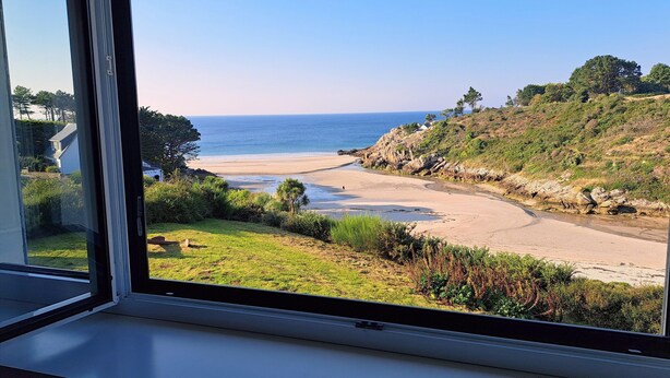 Vista costera desde una ventana, que incluye una playa, el océano y vegetación.