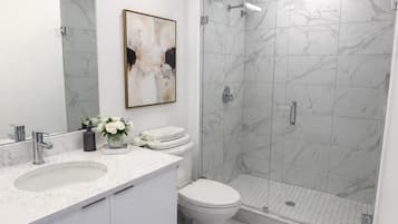 Une salle de bain moderne avec un lavabo en marbre, des toilettes, une douche avec des portes en verre et un grand miroir.