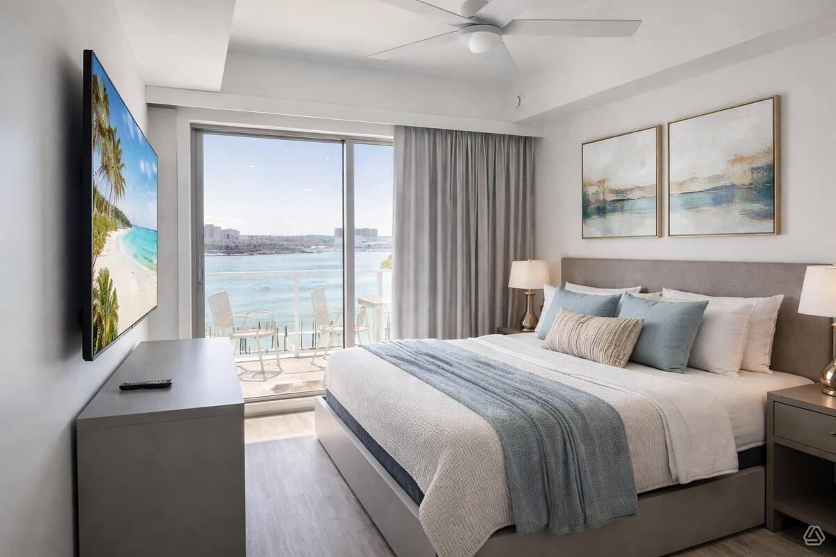 Una habitación de hotel moderna con una cama grande, televisión, balcón con vistas al agua y obras de arte en las paredes.