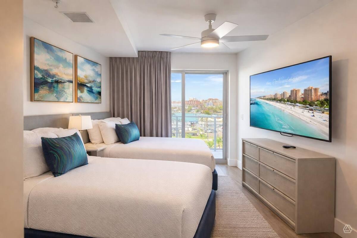 Habitación de hotel con dos camas, televisión, ventilador de techo y ventana grande con vista a la ciudad.