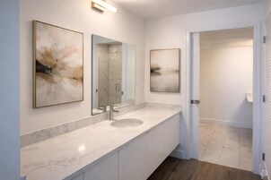 A modern bathroom with a marble sink, two wall-mounted mirrors, and abstract artwork.