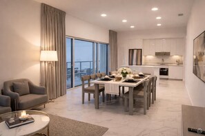 A modern dining area with a table set for four, a sofa, a coffee table, and a view of the city through large windows. - CW Hotel (Clearwater Beach)