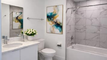 A modern bathroom with a white vanity, a toilet, a bathtub, and abstract art on the walls.