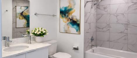 A modern bathroom with a white vanity, a toilet, a bathtub, and abstract art on the walls.