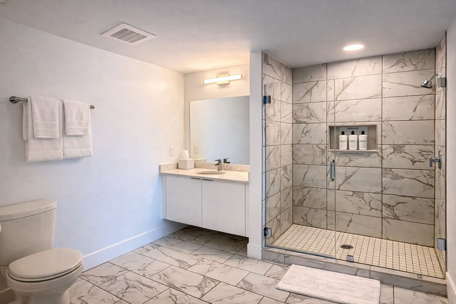 Une salle de bain équipée de toilettes, d’un lavabo, d’un miroir et d’une douche aux parois recouvertes de carreaux de marbre.